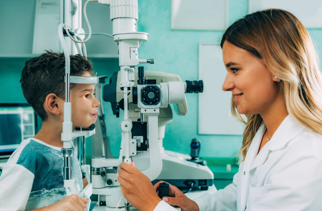 Young boy having eye exam while laying chin on machine with optometrist present