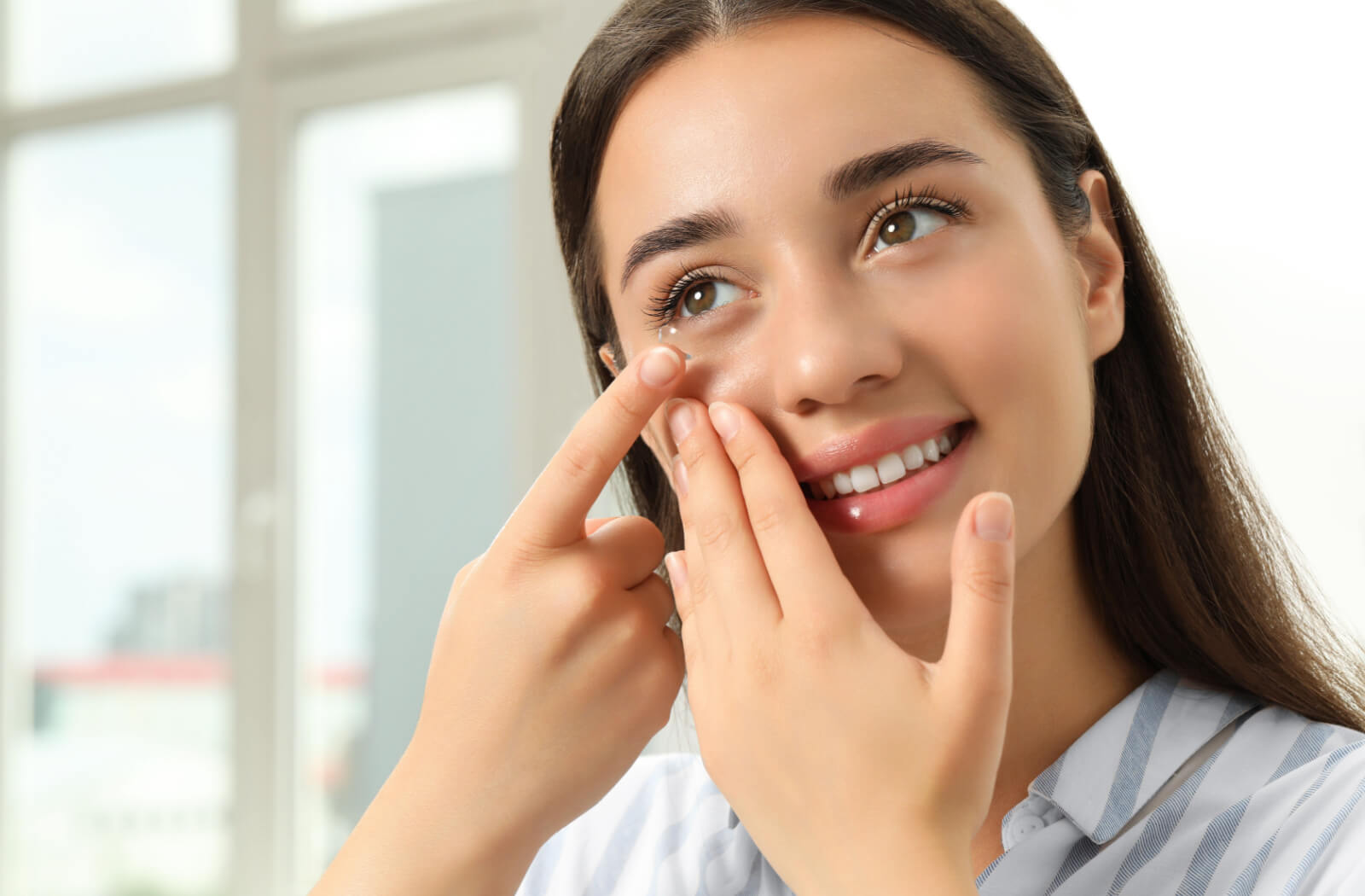 A woman putting soft contact lenses in her eye at home.